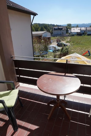 Un balcon avec une table et une chaise, donnant sur un quartier résidentiel avec des maisons et un ciel dégagé.
