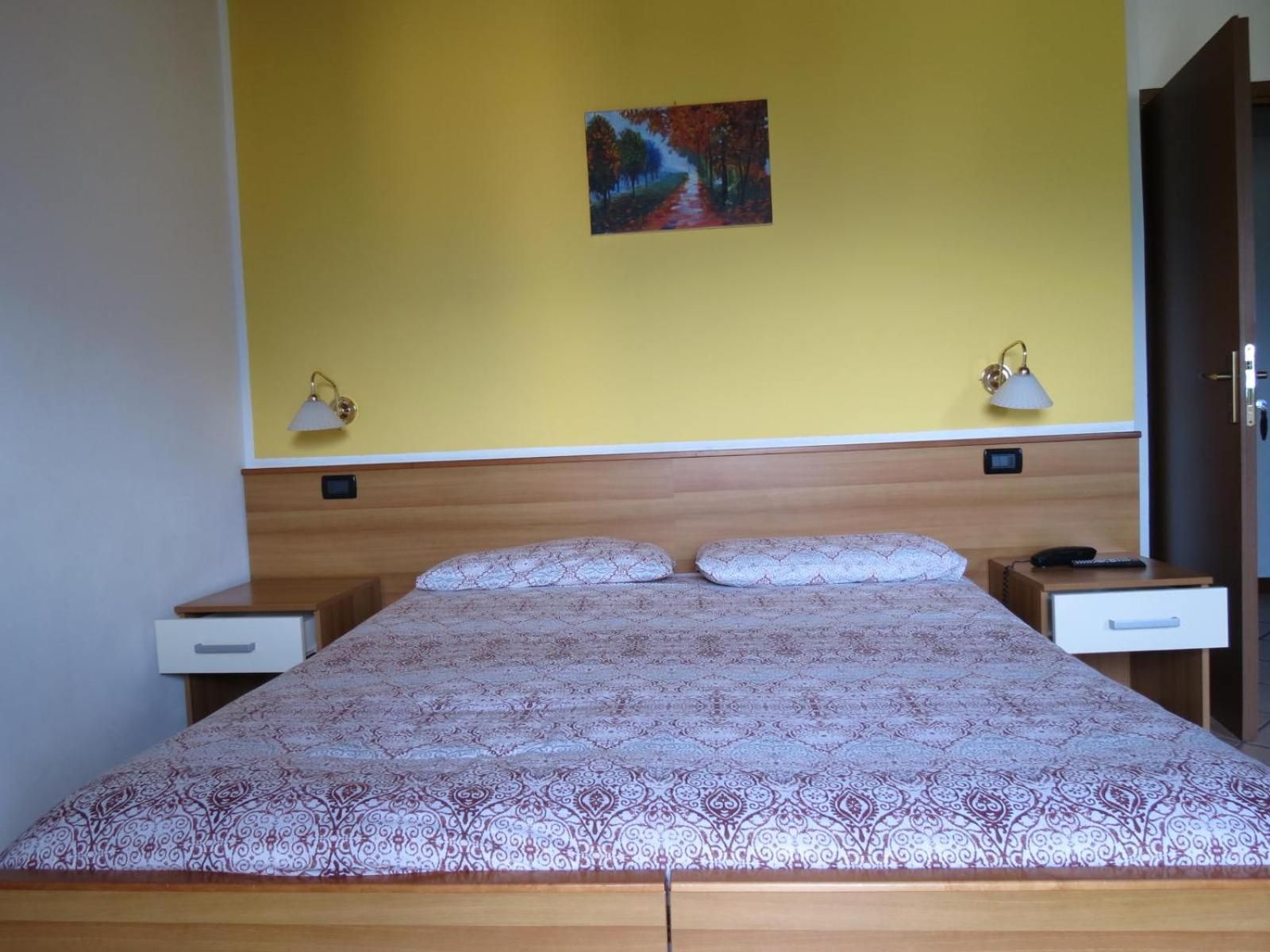 A bedroom with a wooden headboard, a patterned bedspread, two bedside tables with lamps, and a small painting on the wall.