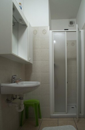 A bathroom with a white sink, a green stool, and a glass-enclosed shower. - Albergo Ristorante Innocenti (Ardenno)