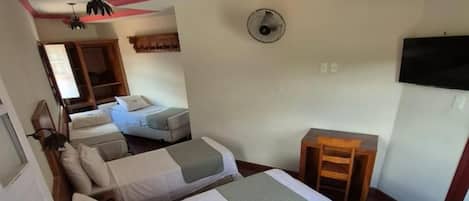 Une chambre d’hôtel avec deux lits, un bureau, une chaise, un ventilateur et un ventilateur de plafond.