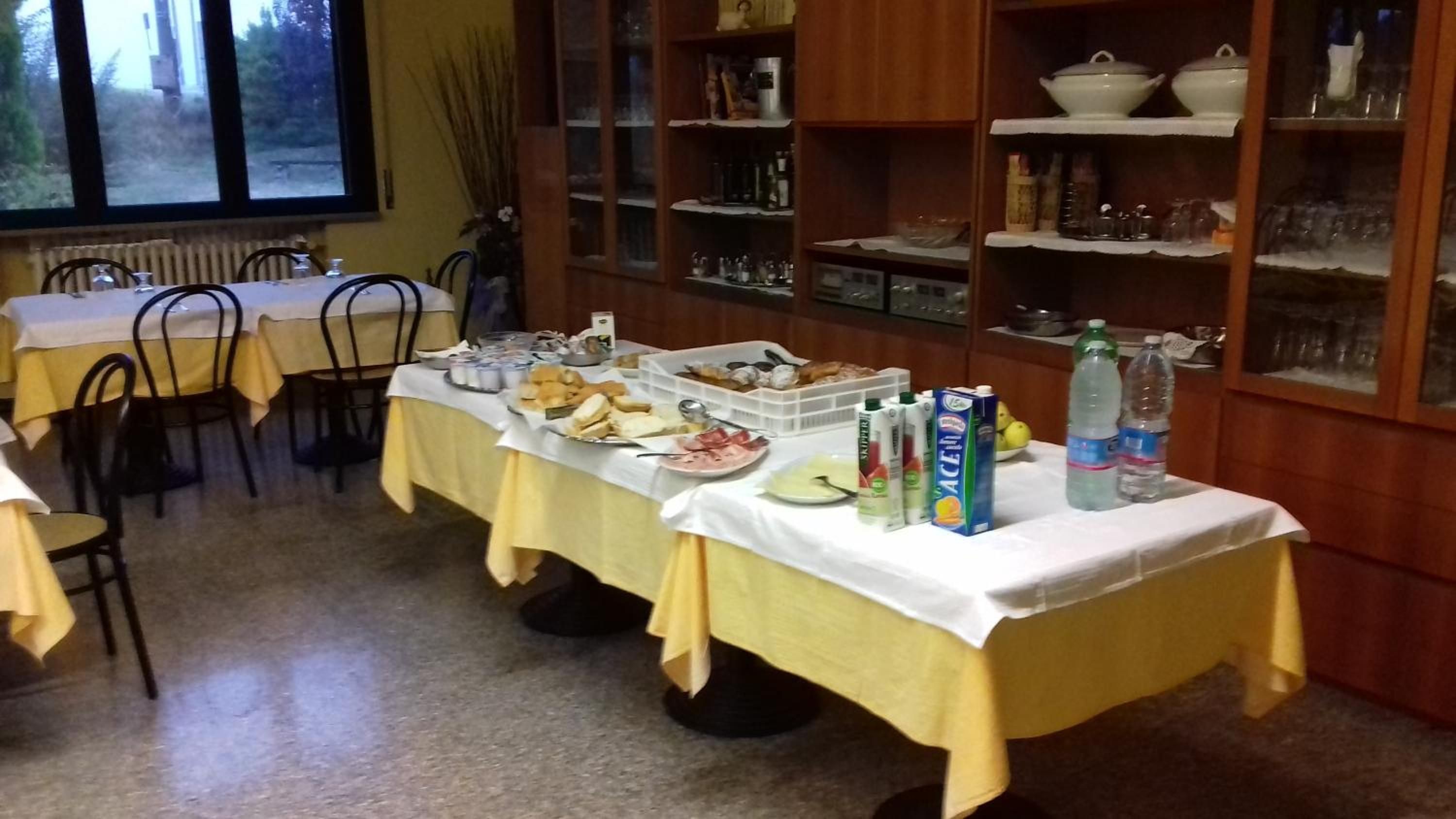 A dining area with tables set for a meal, a buffet with various food items, and a kitchen area with shelves stocked with kitchenware.