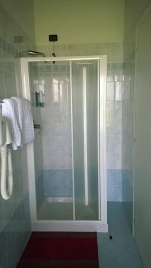 A shower with a glass door, a towel rack with towels, and a red mat on the floor. - Albergo Del Po (Parma)