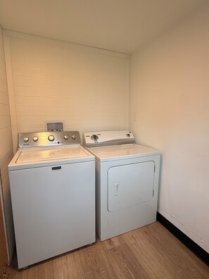 A laundry room with two white Maytag washers and dryers, wooden flooring, and white walls.