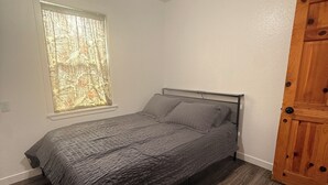 Quarto com cama, ventilador de teto, janela com vista e porta de madeira.