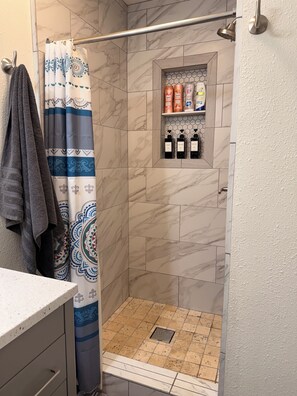 Un espace douche agrémenté d’un rideau de douche à motifs, d’une étagère contenant des articles de toilette et d’un sol carrelé.