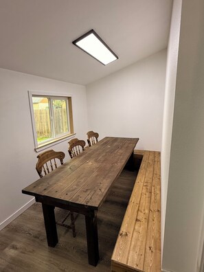 Une pièce avec une longue table en bois, quatre chaises, un banc, une fenêtre et un luminaire au plafond.