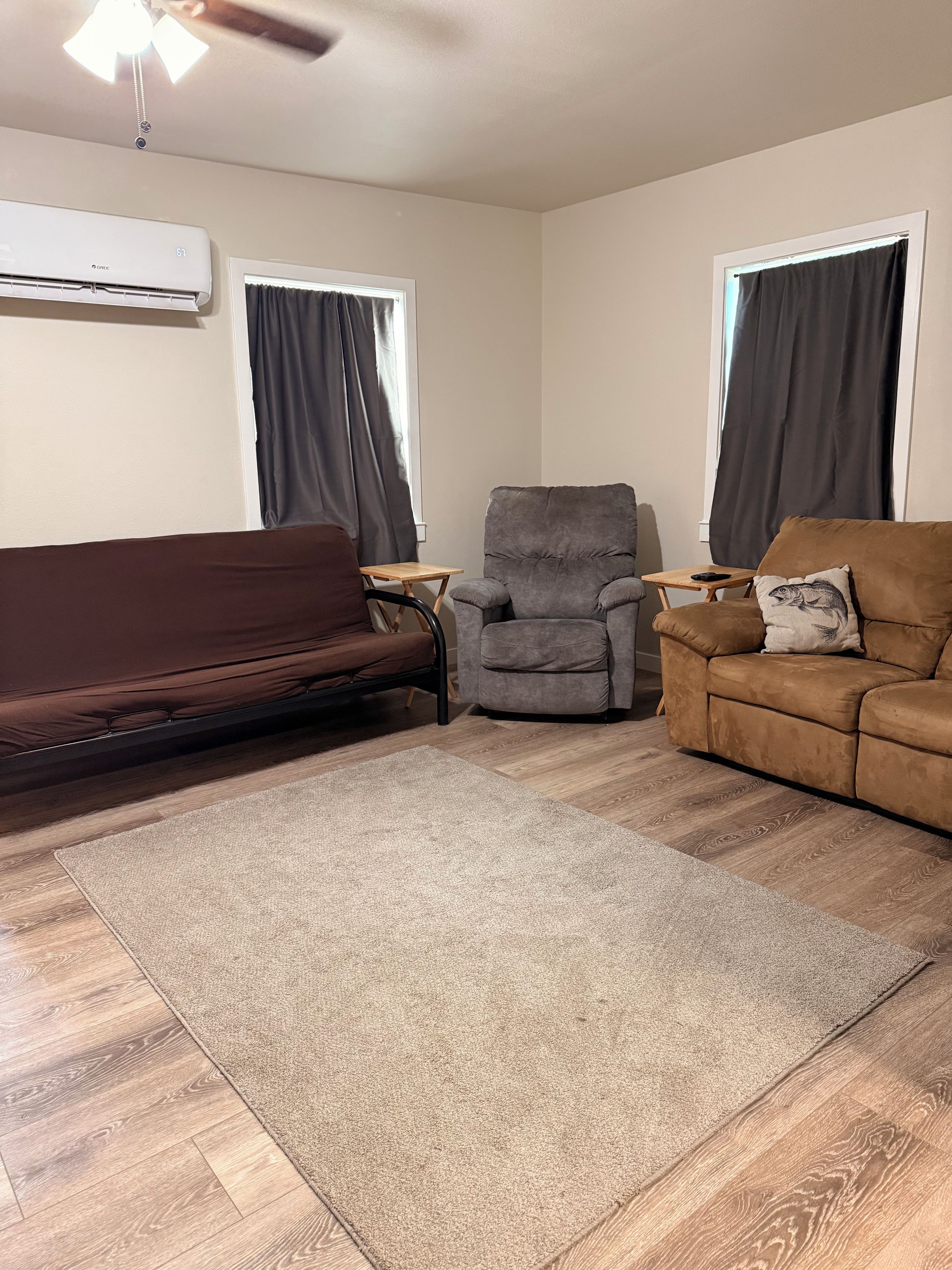 Ein Wohnzimmer mit braunem Sofa, einem grauen Sessel, einer braunen Couch, einem kleinen Holztisch und einem grauen Teppich.