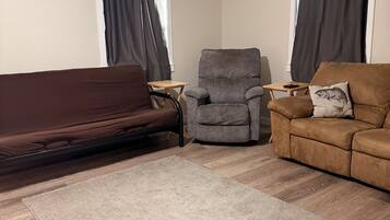 Ein Wohnzimmer mit braunem Sofa, einem grauen Sessel, einer braunen Couch, einem kleinen Holztisch und einem grauen Teppich.