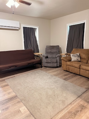 Un salon avec un canapé marron, un fauteuil gris, un divan marron, une petite table en bois et un tapis gris.