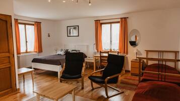 Habitación de hotel con cama, dos sillas, una mesa, escritorio, espejo y ventana con cortinas.