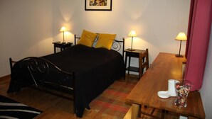 Un dormitorio con una cama, dos mesitas de noche, una mesita auxiliar, una mesa de madera, una silla, una alfombra y un cuadro en la pared.