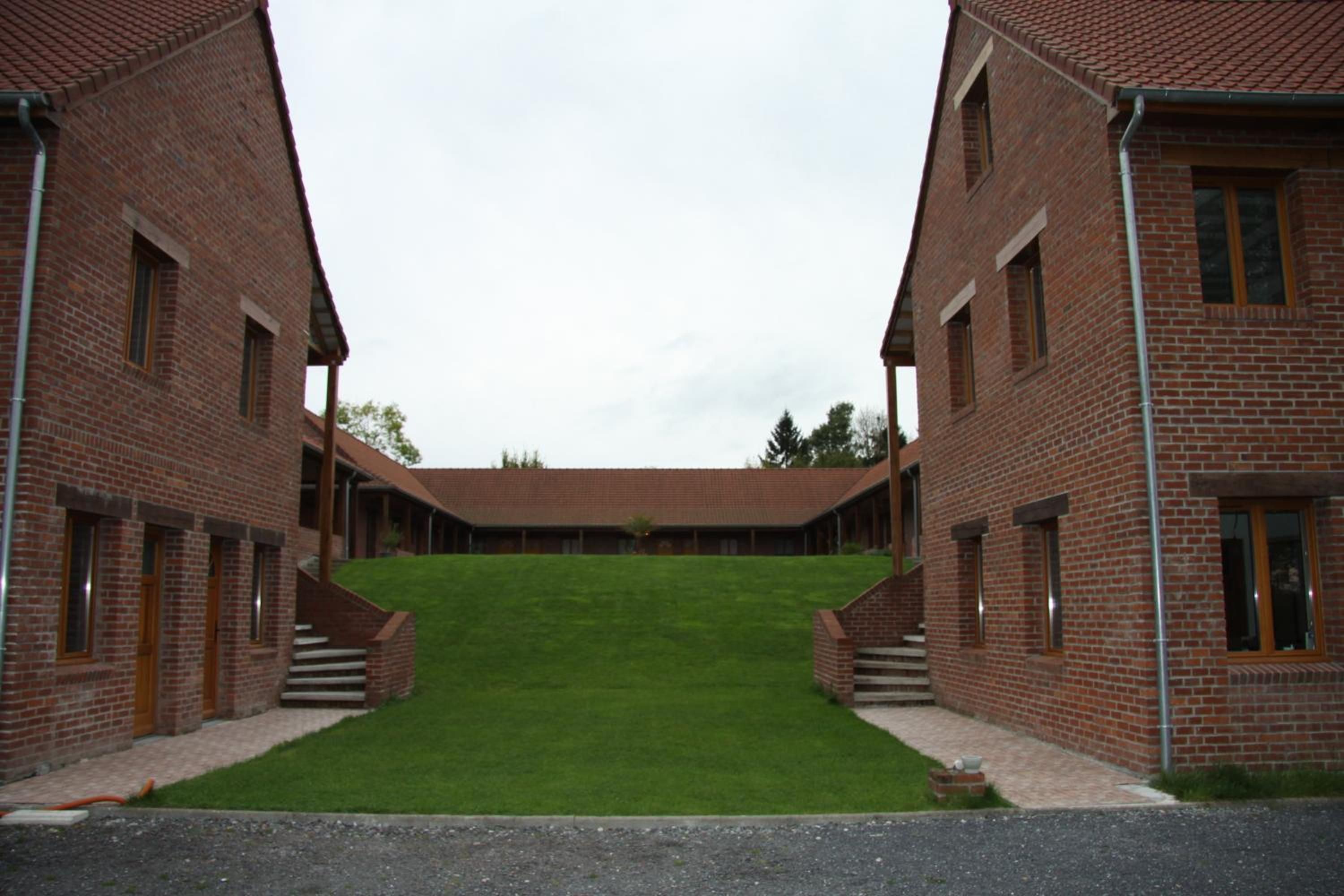 Ein symmetrisches Gebäude mit einer zentralen Rasenfläche, Backsteinmauern und einem Flachdach.
