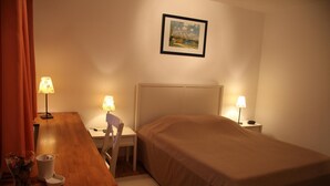 Una habitación de hotel con cama, escritorio, dos lámparas, una silla y un cuadro en la pared.