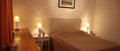 Une chambre d’hôtel avec un lit, un bureau, deux lampes, une chaise et un tableau au mur.