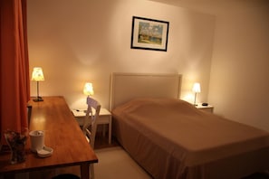 Una habitación de hotel con cama, escritorio, dos lámparas, una silla y un cuadro en la pared.