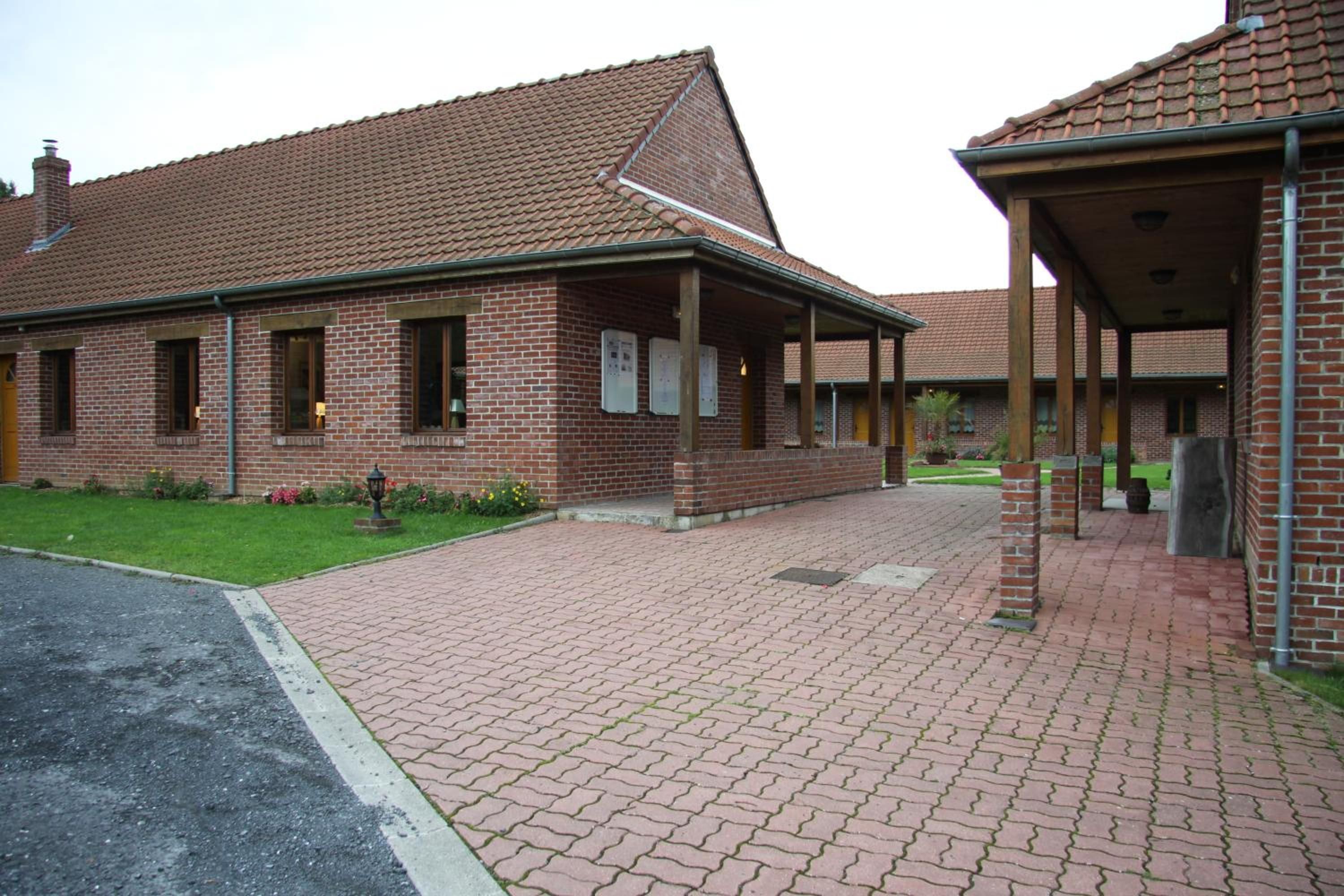 A brick building with a tiled roof, a covered walkway, and a paved entrance area.