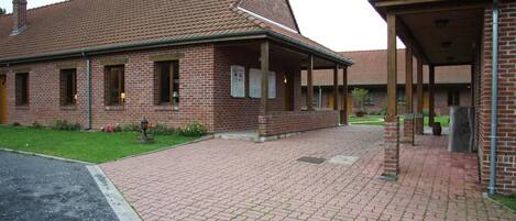 A brick building with a tiled roof, a covered walkway, and a paved entrance area.