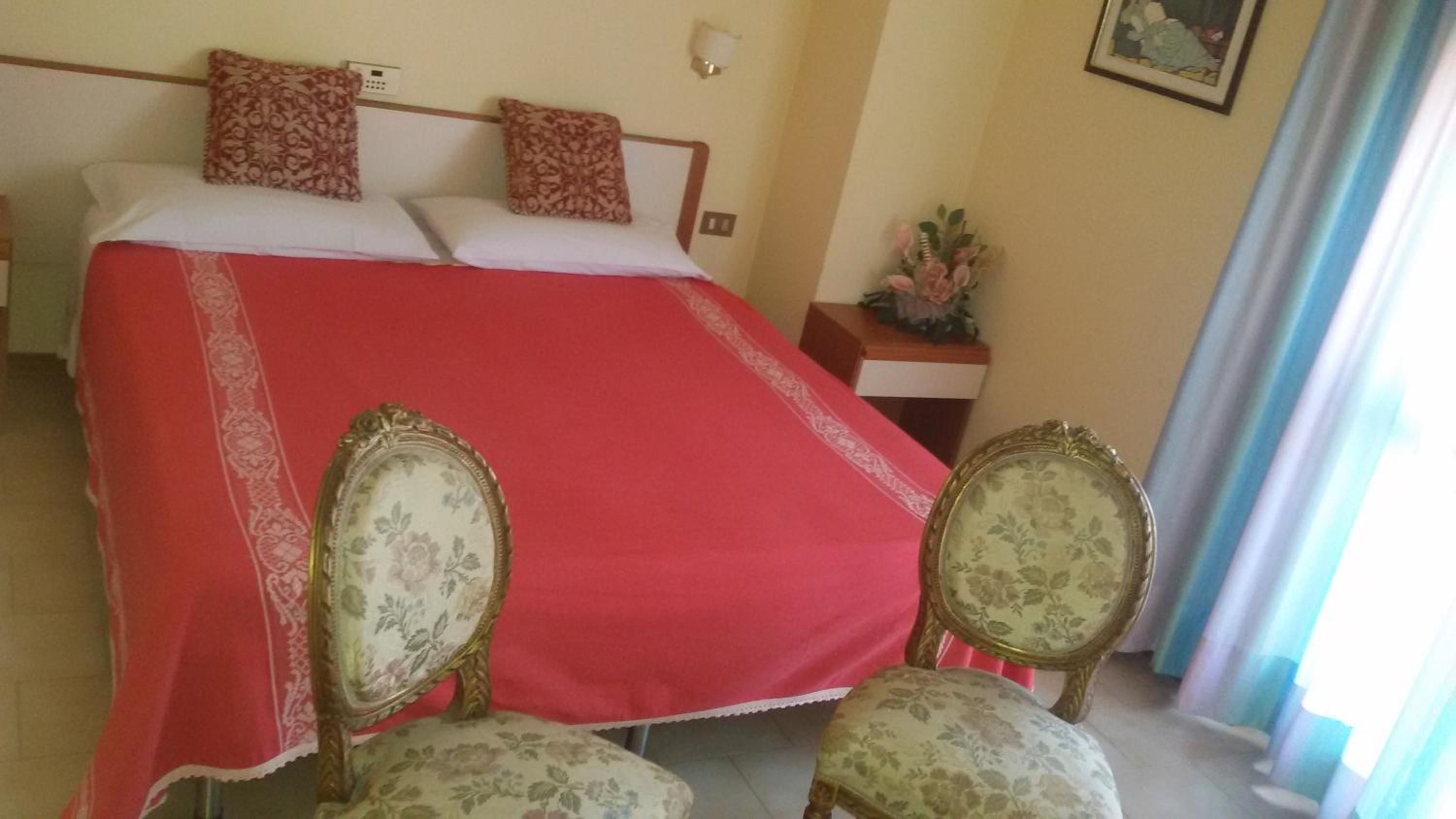 Una camera d'albergo con un letto, due poltrone, un comodino e una lampada a parete.