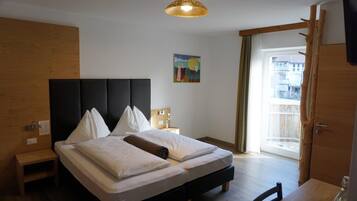 Una camera d'hotel con un letto grande, un comodino, un tavolino, un quadro appeso e vista attraverso una porta.