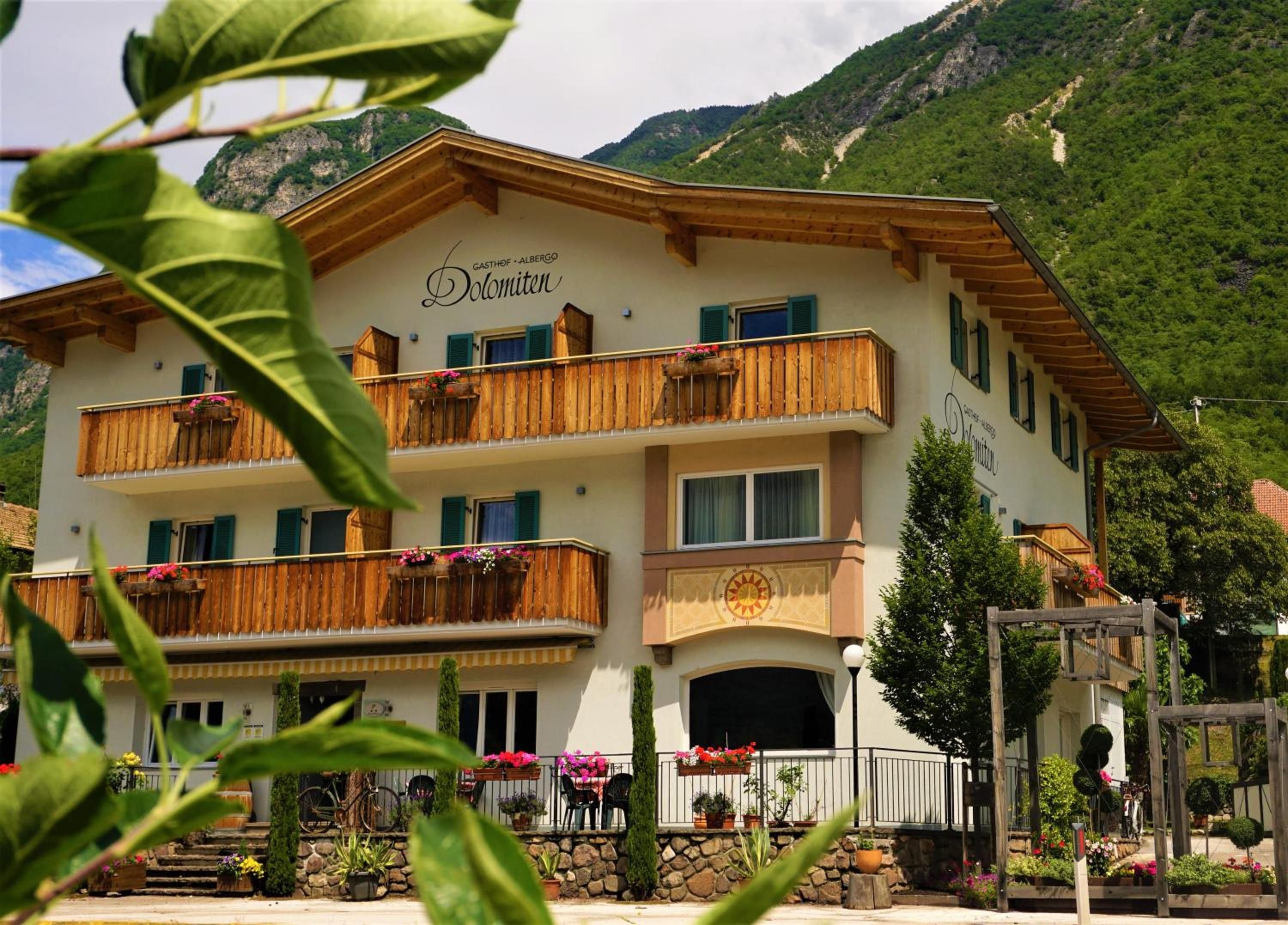 A multi-story building with balconies, a stone facade, and a mountainous backdrop.