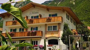 A multi-story building with balconies, a stone facade, and a mountainous backdrop.
