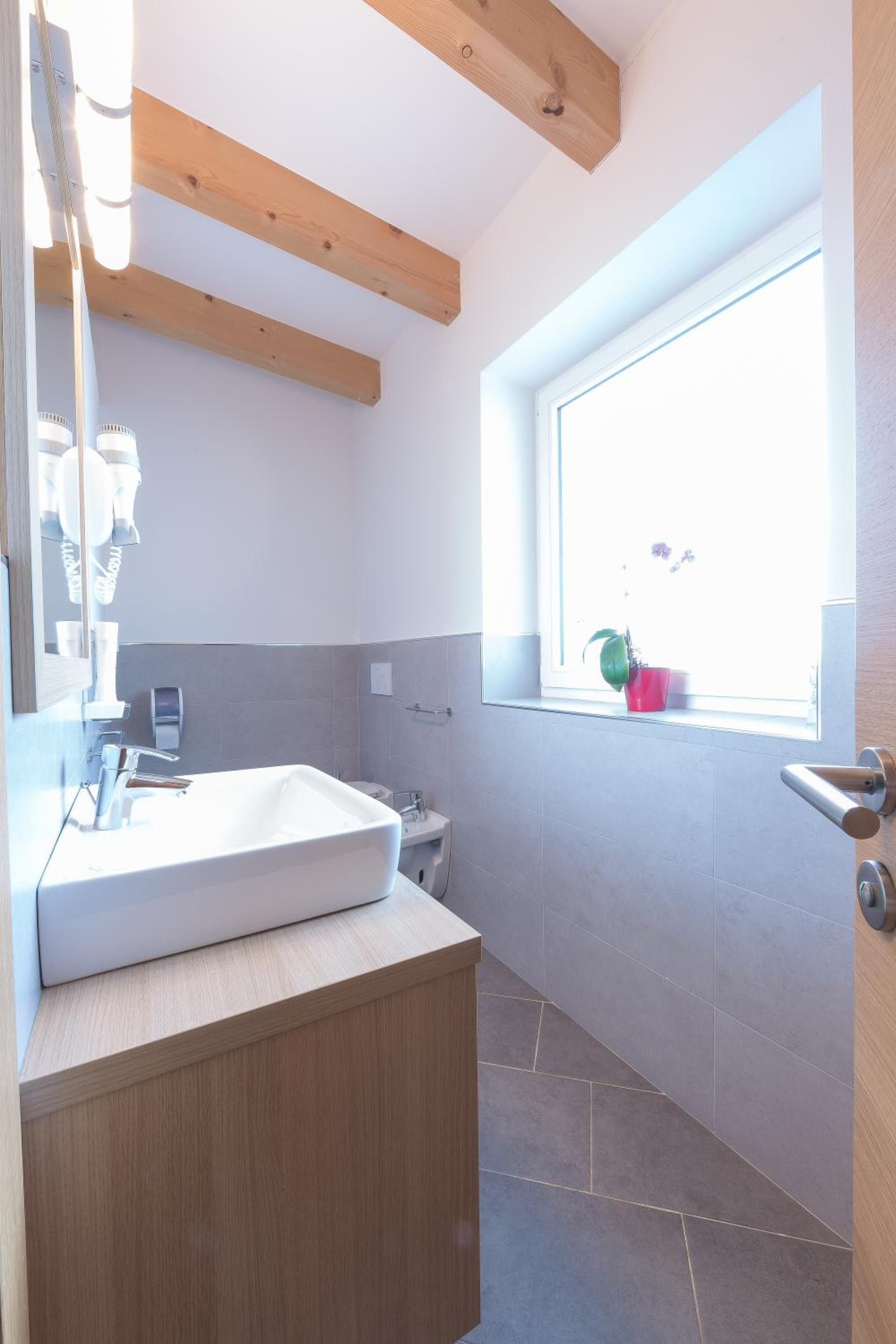 Un bagno moderno con un'ampia finestra, un lavandino bianco e travi in legno al soffitto.