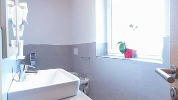 Un bagno moderno con un'ampia finestra, un lavandino bianco e travi in legno al soffitto.