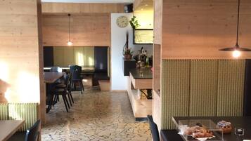 Un interno moderno con pavimento in pietra, pareti rivestite in legno e un'area pranzo con tavoli e sedie.