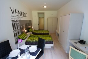 Habitación de hotel con dos camas, un área de comedor con una mesa dispuesta para dos personas y una pared con una imagen impresa.