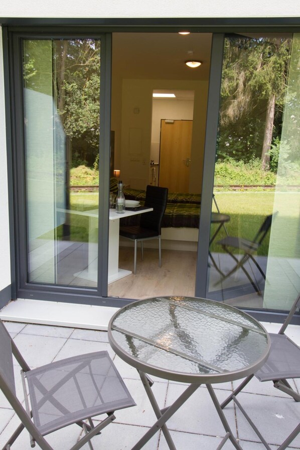 Una habitación moderna con puerta de vidrio que da a un comedor, una mesa redonda de vidrio y dos sillas.