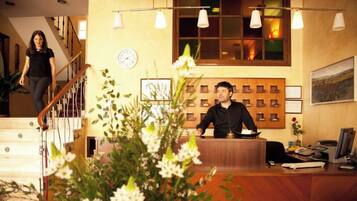 A reception desk with a clock, framed pictures, and a plant in the foreground.