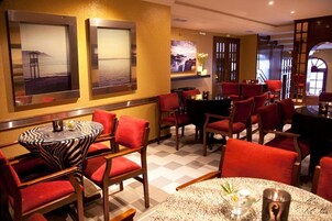Un comedor de hotel con sillas tapizadas rojas, mesas redondas y cuadros en las paredes.