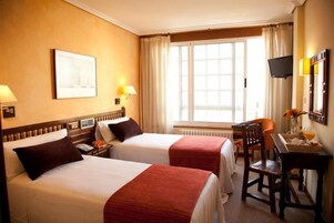 Habitación de hotel con dos camas, un escritorio, una silla, un televisor y una ventana con cortinas.