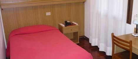 A hotel room with a bed, a desk, a chair, a nightstand, and a lamp.