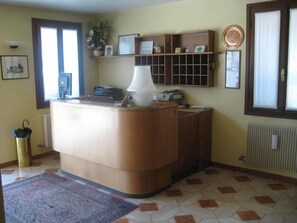 A room with a reception desk, a potted plant, a framed certificate, and a radiator. - Hotel Ristorante Dotto (Maserada sul Piave)