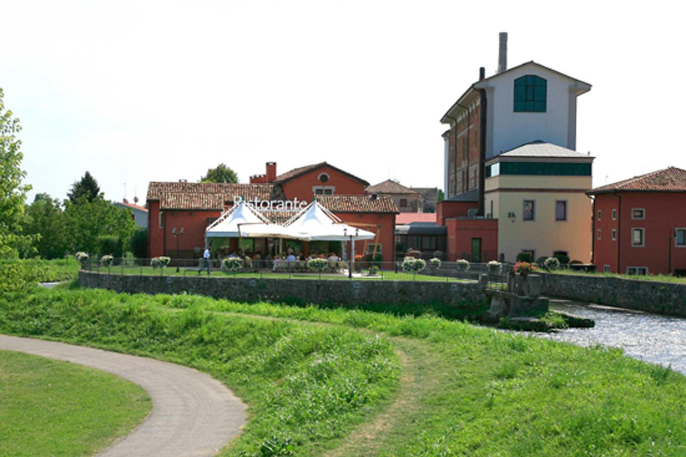 A riverside setting with a building featuring a prominent tower and a restaurant with outdoor seating.