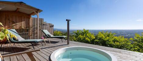 Una terraza de madera con un jacuzzi, sillas de descanso y una estructura de madera.