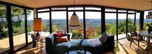 Una habitación con un muro de vidrio curvo, un sofá, una mesa y sillas, con vista a un paisaje.