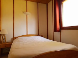 Una cama individual en una habitación con paneles de madera y una ventana con cortinas rojas.