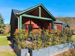 Una cabaña de madera con techo verde y un porche cubierto.