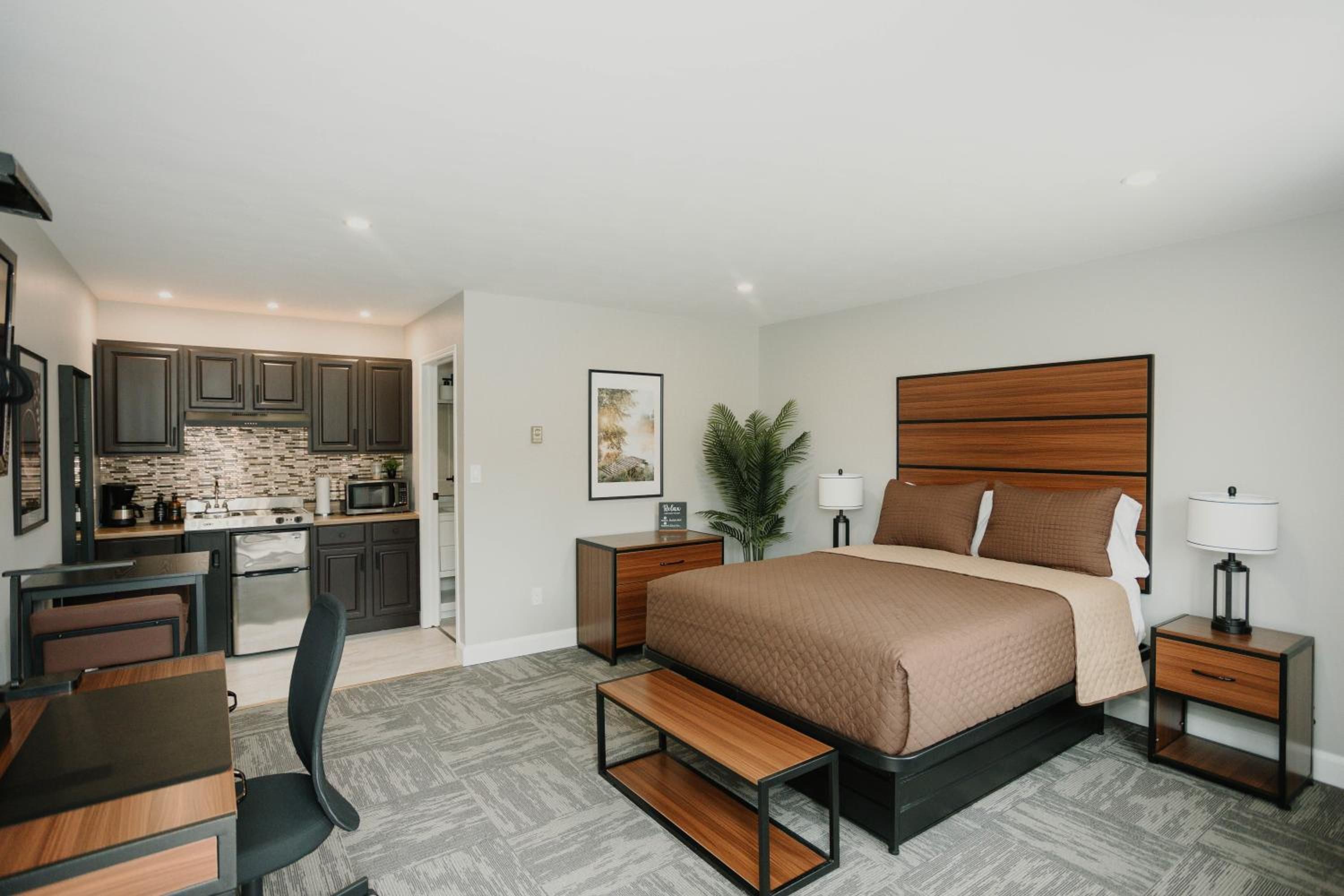 A modern bedroom with a large bed, bedside tables, a desk, and a kitchenette.