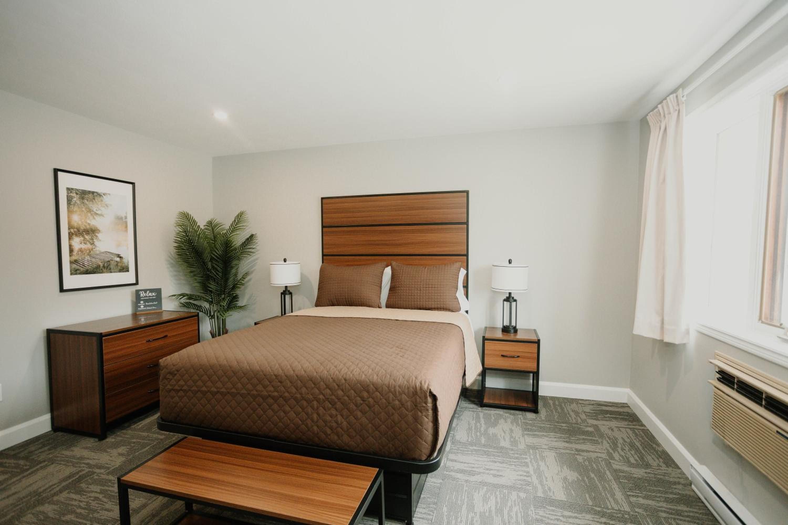 Une chambre d’hôtel avec un grand lit, des tables de chevet, un bureau, une chaise, une plante en pot et une fenêtre avec des rideaux.