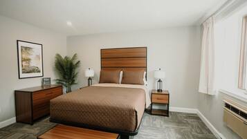 Une chambre d’hôtel avec un grand lit, des tables de chevet, un bureau, une chaise, une plante en pot et une fenêtre avec des rideaux.