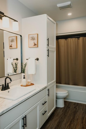 A modern bathroom with a white vanity, a large mirror, a toilet, and a shower curtain.