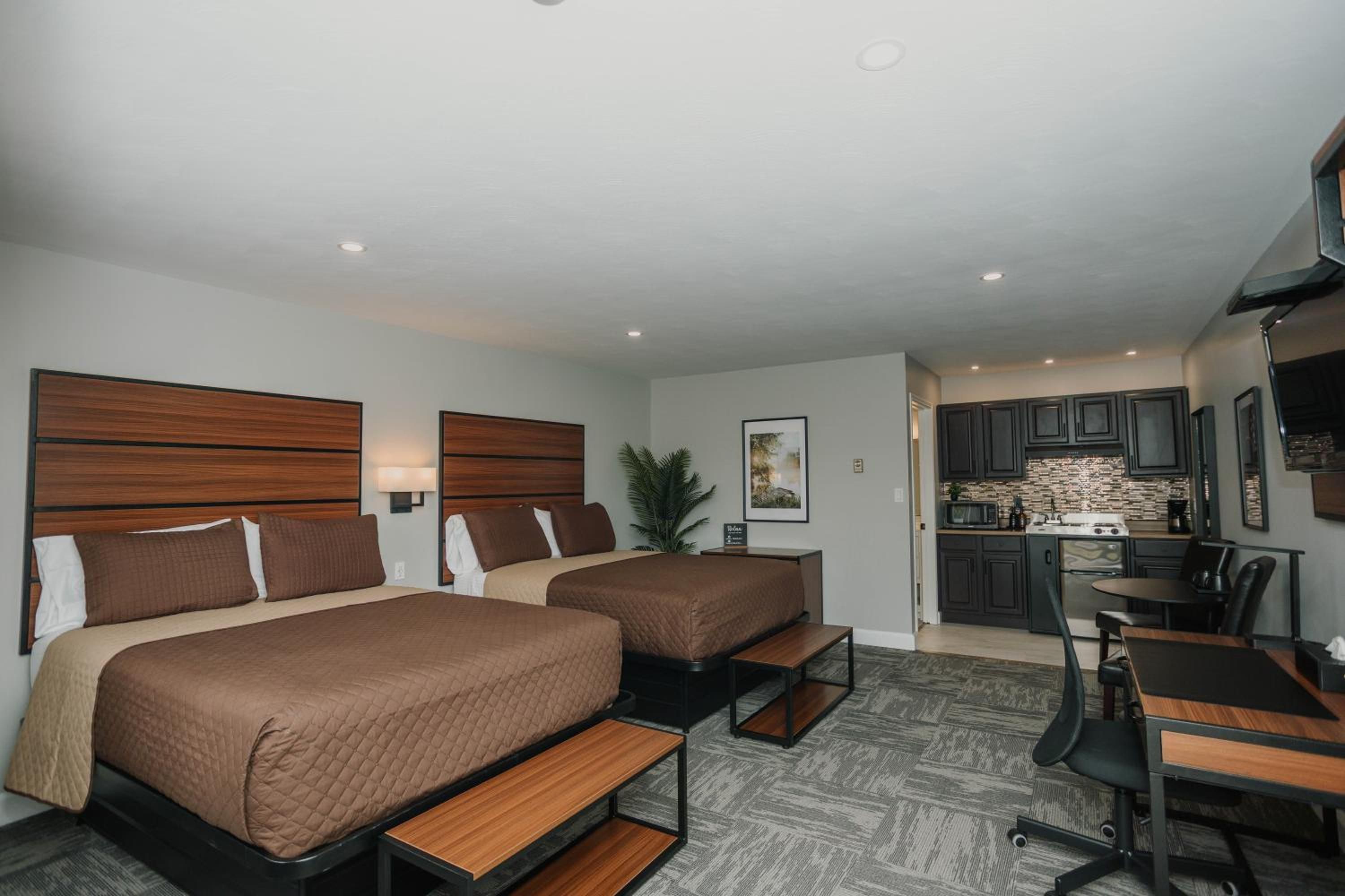 Une chambre d’hôtel avec deux lits, un bureau, une chaise, une kitchenette et une petite table à manger.