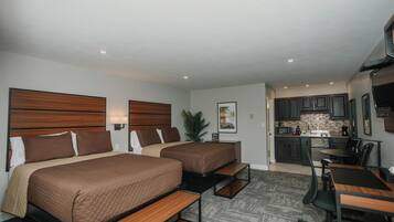 Une chambre d’hôtel avec deux lits, un bureau, une chaise, une kitchenette et une petite table à manger.