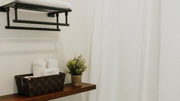 A bathroom with a white toilet, a shelf with a plant and a basket, and a white shower curtain.