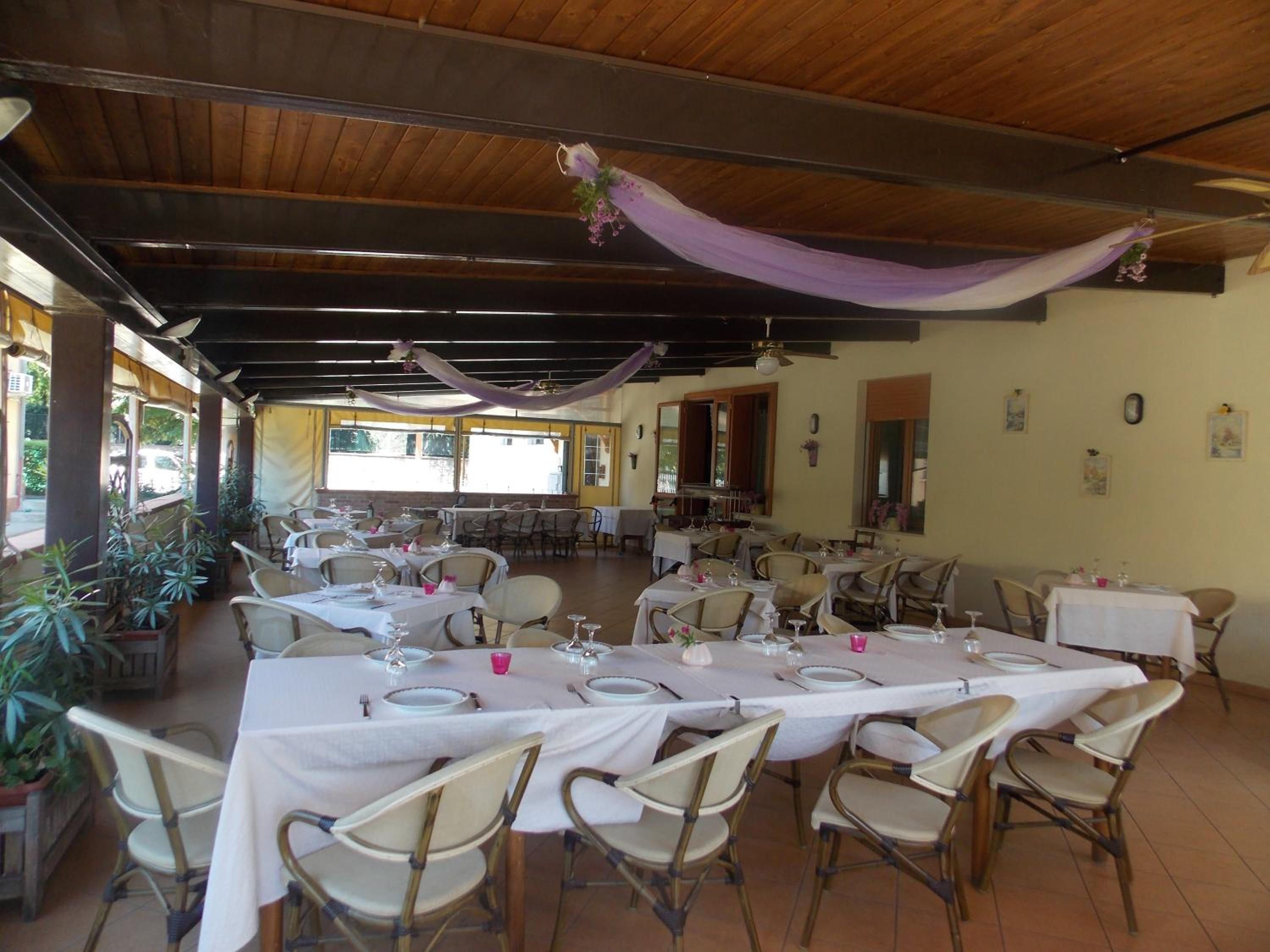 An indoor dining area with tables set for multiple guests, chairs arranged around them, and a ceiling with exposed beams.