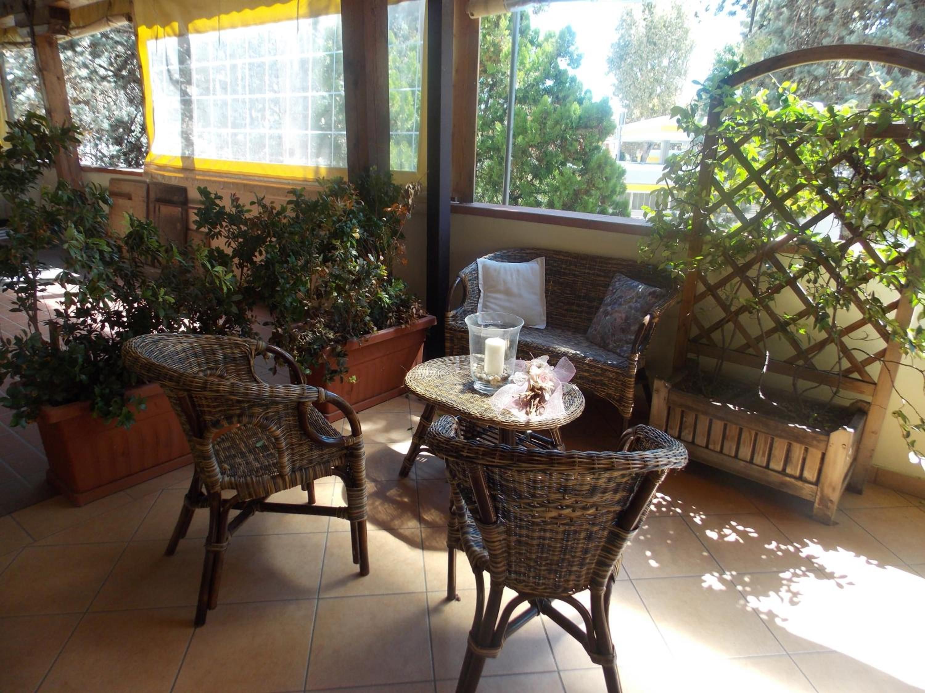A covered outdoor seating area with wicker furniture, a table with a candle, and potted plants.