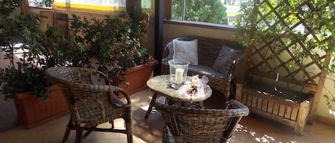 Un espacio exterior techado con mobiliario de mimbre, una mesa con vela y plantas en macetas.